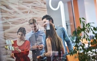 A group of four professionals stand together talking in a conference room setting.