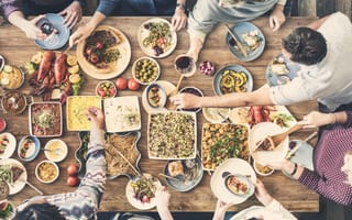 An aerial-view image of friends gathered around a table eating and drinking together.