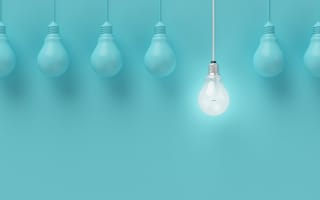 Image of a lightbulbs hanging in a row. Only one is illuminated and the rest are covered in blue paint to match the background behind them.