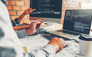 Image of two data science co-workers sitting in front of computers, discussing and collaborating on code.