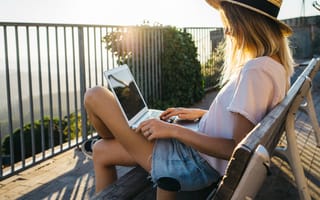 Image of a woman sitting out on a balcony doing work on a laptop as the sun sets