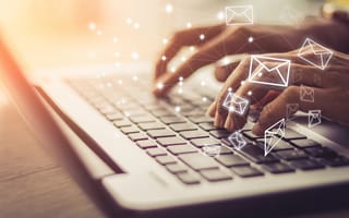 Hands typing on laptop keyboard with mail icons floating above