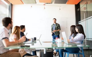 A San Francisco sales team meets around a table as one man presents at a white board