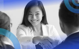 A job candidate shakes hands with an interviewer as another looks on across a table
