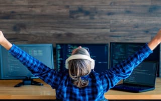A software developer in front of three monitors taking a break from work to stretch.