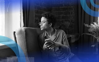 A Black woman gazes pensively out a window, her phone forgotten in her hands. /wearables/daydreaming-augmented-reality