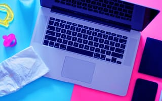 A laptop surrounded by both baby items and work items as a new parent goes back to work.