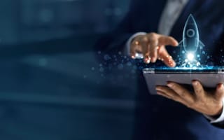 A person uses a laptop to launch a holographic rocket from a tablet