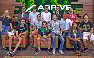 Arrive Logistics team photo with the company logo on the wall behind them