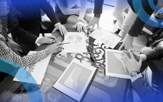 A group of people work on tables and charts at a large table.