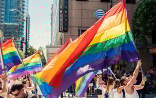 People walk through the street with the Pride flag held over their heads