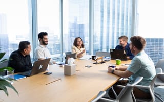 A group of Pricefx employees hold a team meeting around a large table in a corner office.