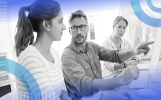 A man points at something on a computer screen while two young women watch. /career-development/tech-apprenticeships
