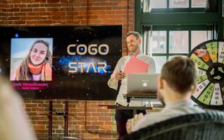 Cogo Labs teammate standing in front of a brick wall and screen presenting to team