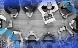 A conference table surrounded by people working on laptops and mobile devices