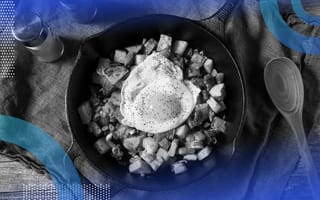 A cast-iron skillet with corned beef hash topped with a fried egg and a wooden spoon next to it.