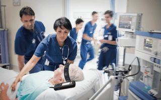 A hospital room with five healthcare workers and an elderly man wearing a Ceribell headband device
