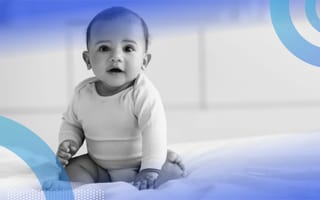 A smiling baby sits on a bed