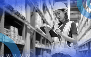 A young woman in a warehouse, wearing a high-visibility vest and hard hat, checks something off on a tablet. /operations/benefits-for-every-employee
