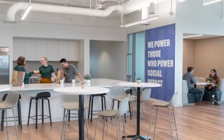 Employees in Bonterra's office. On the right there are two employees at a table. On the left there are three in the kitchen. Between is a wall that reads "WE POWER THOSE WHO POWER SOCIAL IMPACT."