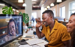 Photo of two colleagues in office waving at a remote coworker on the computer screen.