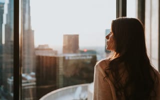 Young woman looking out window at downtown Los Angeles' tall buildings.