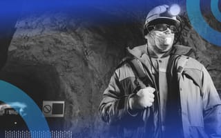 A miner wearing a mask and safety gear stands in an underground mine