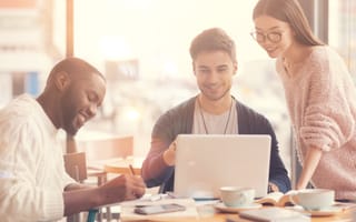 Three colleagues smile around a laptop