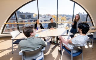 Five people sit around a table in front of a semicircle window
