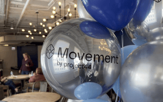 A cluster of metallic balloons emblazoned with the Movement logo.
