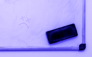 An old, dirty whiteboard with a dead smily face drawn on it.