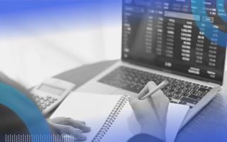 A person looks at stock prices on a laptop and takes notes in a notebook