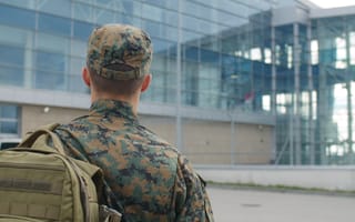 A service member in fatigues with his back to us walks toward a glass facaded building