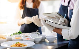 Three chefs writing recipe in a notebook with food plated on a table in front of them
