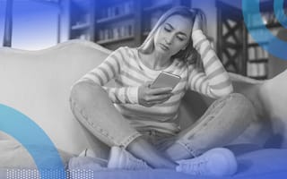 A woman sits on the couch and frowns while looking at her phone
