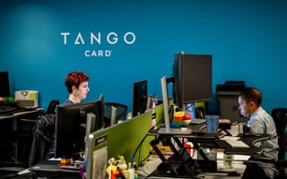 Two Tango Card employees at work under a blue wall and the Tango Card logo.