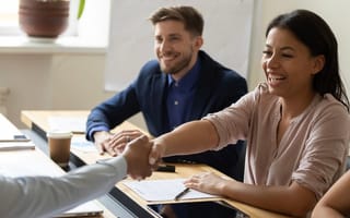 A Black woman smiles and shakes hands with someone across the table