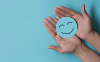 Hands against a teal background, holding a teal smiley face