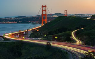 A long exposure photo of cars crossing the Golden Gate Bridge at dusk.