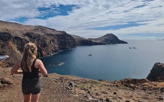 Partner Delivery Consultant Kaitlin Fox with her back to the camera, standing on a cliff overlooking water.