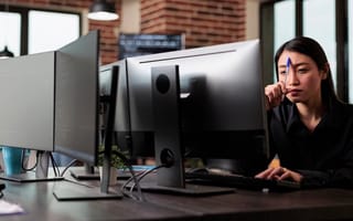 A woman holds a pen to her forehead as she concentrates on her computer