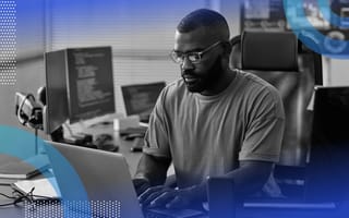 back-end development image of a man sitting at a laptop wearing glasses. He has a desktop computer and another laptop in the background. You can see code on the screen.