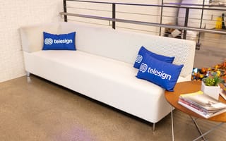 A white couch with several Telesign pillows on it.