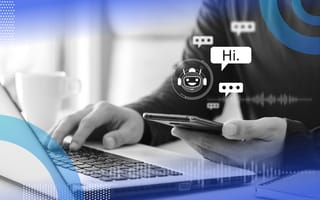 Natural Language Processing (NLP) image of a person's hands. One is on a laptop and the other holds a smartphone. There are chat icons hovering above the smart phone as if the person is engaging with a chat bot.