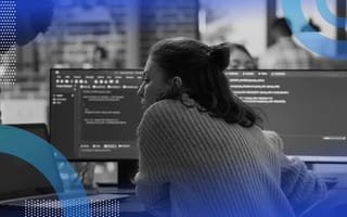 Python algorithms image of a woman shot from behind. She looks intently at two computer screens in front of her that are full of code.