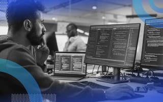 Image of a bearded man looking intently at three monitors with code on them.