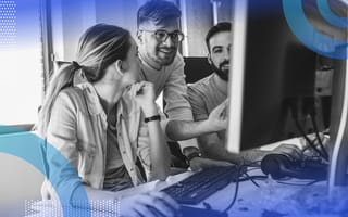 R Programming Language Image of two men and a woman working together. in front of a desktop computer. The woman looks back at the man who is smiling and pointing at the comptuer.