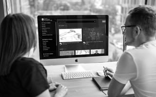 A woman and man sit at a Mac desktop