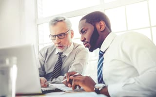 An employee and a manager sit side-by-side looking at a laptop.