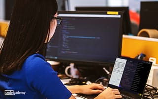 Photo of woman at laptop with separate monitor working on code